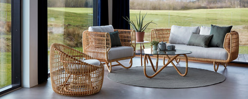 Hyggelig loungemøbler med rattanmøbler, myke puter, et glassbord og dekorative planter som skaper en stilfull og innbydende atmosfære.