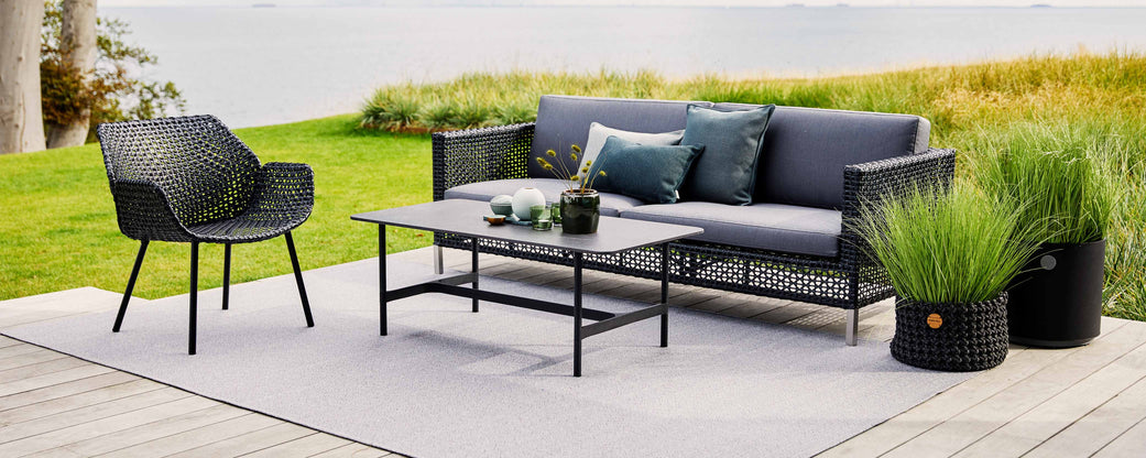 Stilfull sittearrangement med en moderne sofa, lenestol og sofabord, supplert med dekorative puter og grønt.