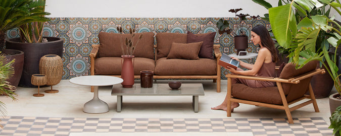 Et koselig sitteområde med brune lenestoler, et kaffebord, planter og dekorative veggfliser som skaper en avslappet atmosfære.