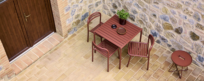 A cozy café setting featuring a square wooden table, chairs, and a small side table, adorned with a potted plant and a coffee cup.