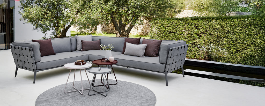 Moderne grå seksjon sofa med lilla puter og et rundt kaffebord i et loungeområde.