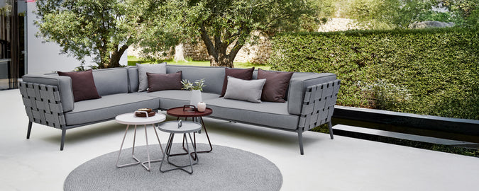 Moderne grå seksjon sofa med lilla puter og et rundt kaffebord i et loungeområde.