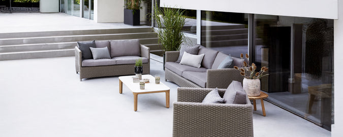Moderne utendørs loungeoppsett med grå sofa, lenestol og hvit bord.