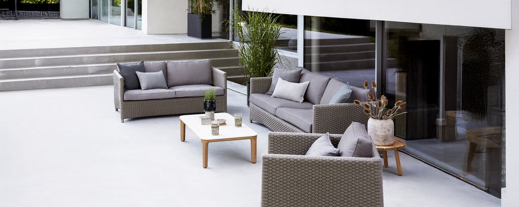 Moderne utendørs loungeoppsett med grå sofa, lenestol og hvit bord.