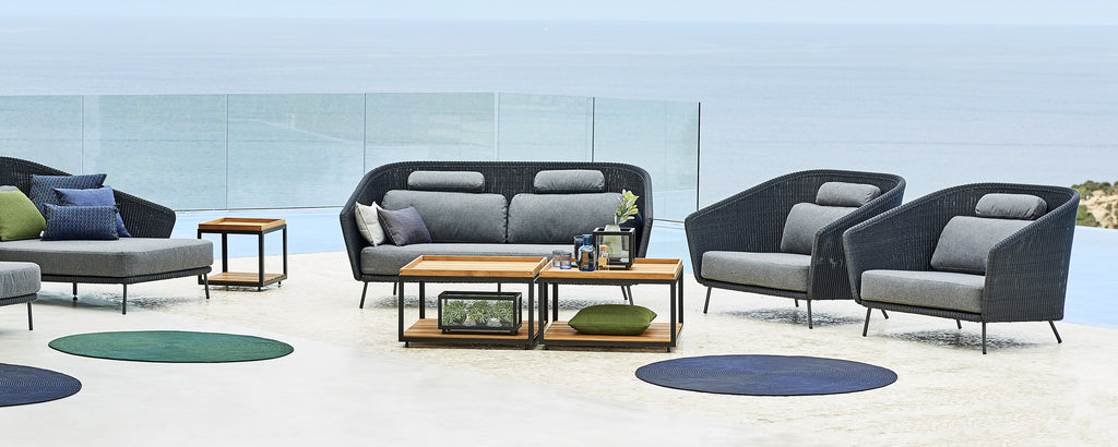 Moderne loungeområde med grå sofa, svarte lenestoler og trebord.