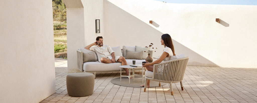 Moderne loungeområde med beige sofa, hvite puter, grå stol og rundt bord.