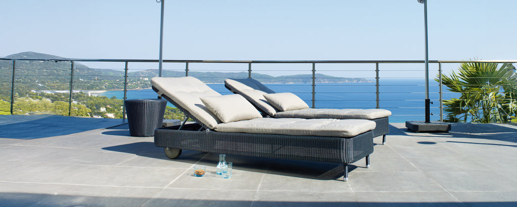 To moderne grå og svarte lenestoler på en terrasse med utsikt over havet.