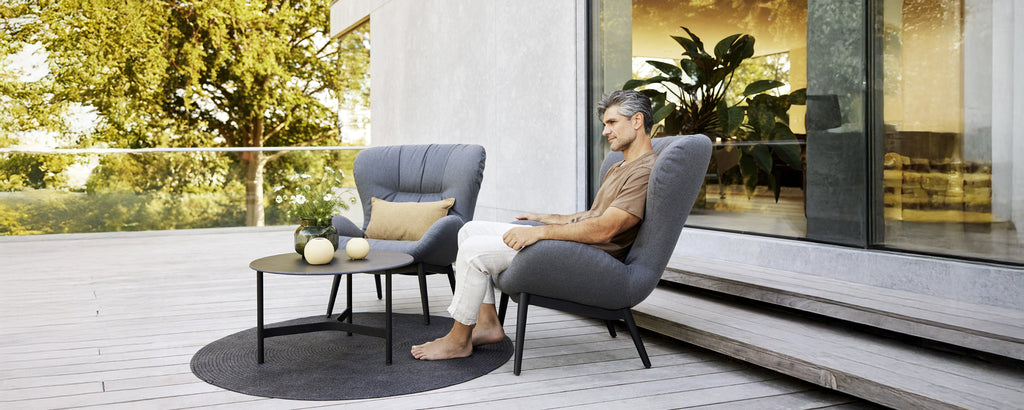 Moderne loungeområde med grå lenestoler, et svart bord og et rundt teppe.