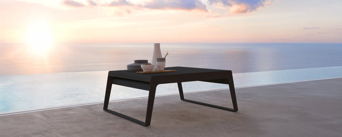Moderne svart bord på en terrasse med utsikt over solnedgangen over vannet.