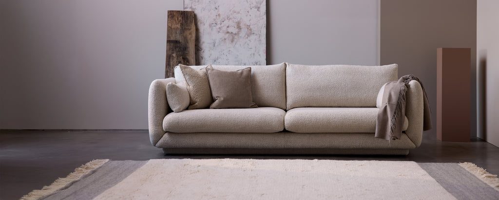 Beige sofa med grå puter i en moderne lounge-setting.
