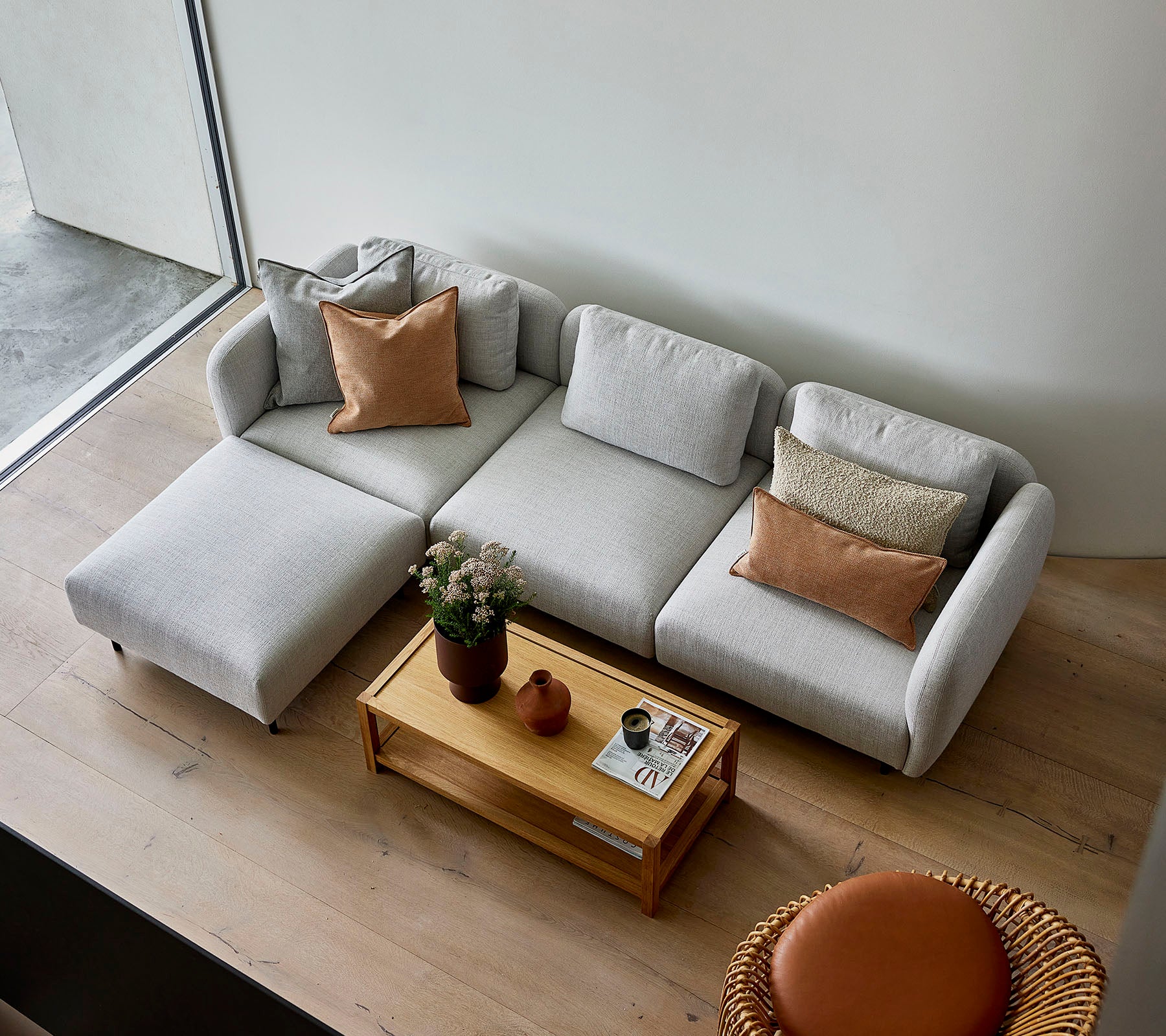 En stilren lys grå modulsofa med puter, kombinert med et trebord og en rund sittemulighet, som skaper en koselig atmosfære.