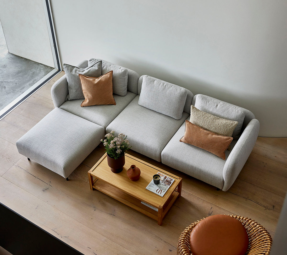 En stilren lys grå modulsofa med puter, kombinert med et trebord og en rund sittemulighet, som skaper en koselig atmosfære.