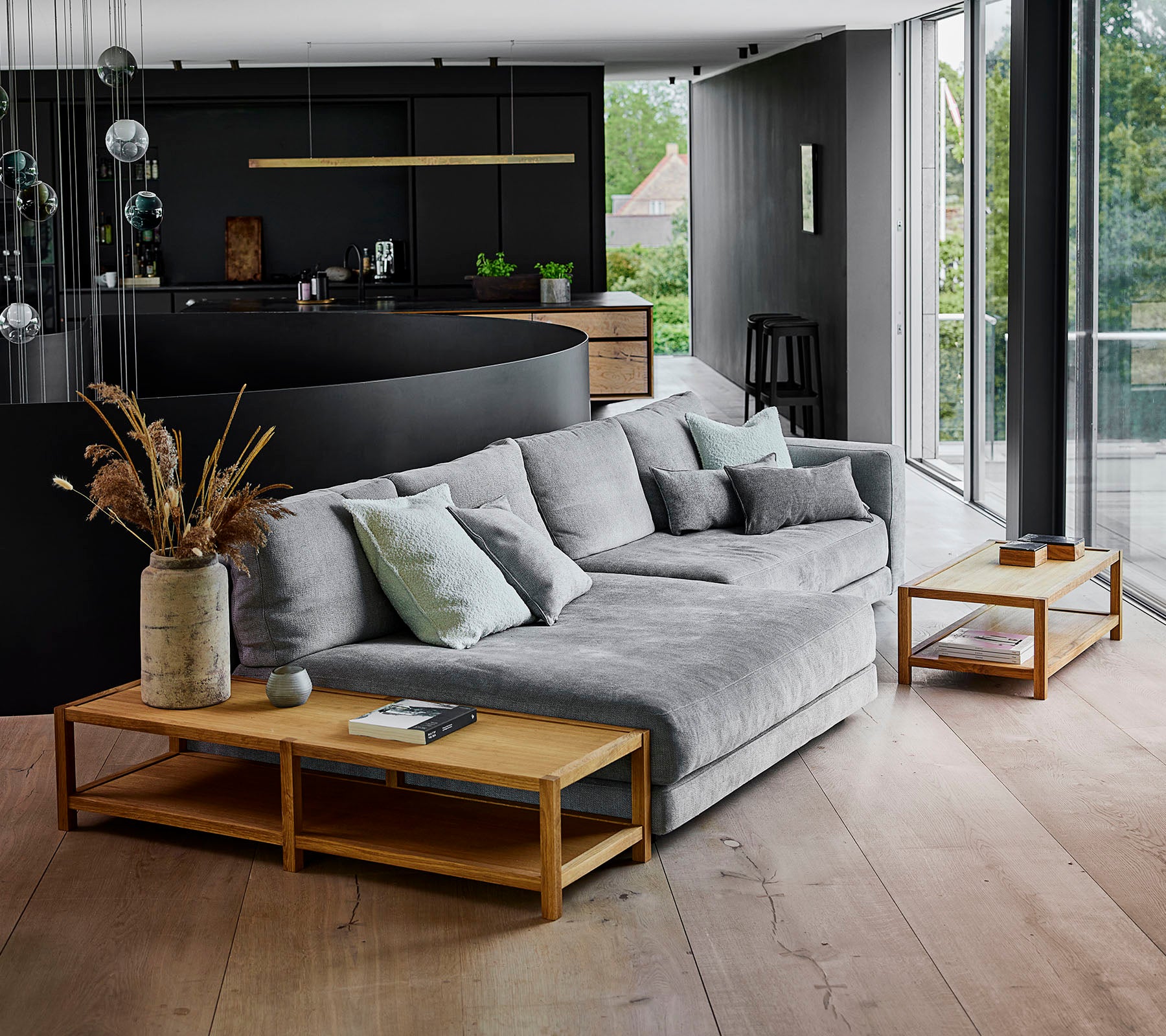 Moderne oppholdsrom med en grå kombinert sofa prydet med puter, komplementert av trebord og dekorative plantearrangementer.