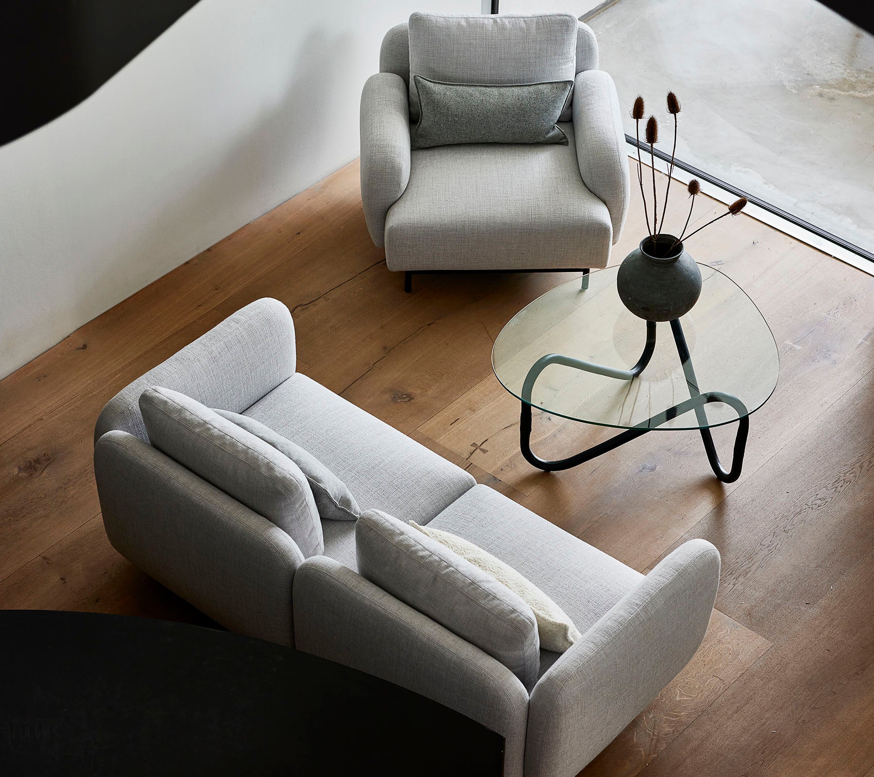 Stilige grå sofaer og et elegant glasskaffebord med dekorative elementer på bordplaten, plassert mot et varmt tregulv.