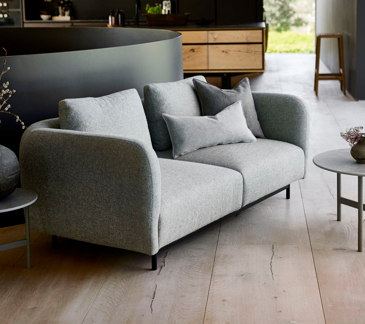 Moderne grå sofa med myke puter, kombinert med et lite rundt bord, satt mot en minimalistisk bakgrunn.