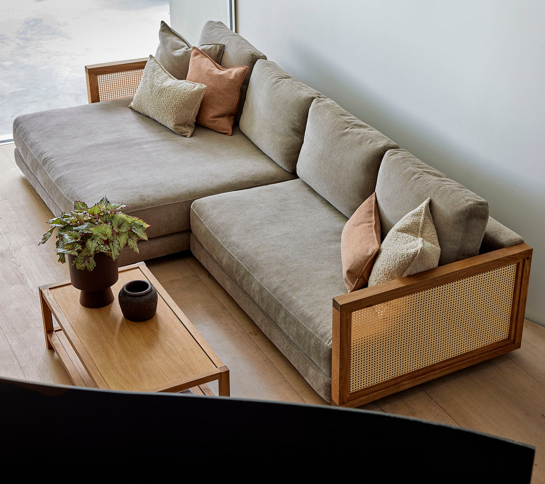 En stilfull seksjonssofa med myke puter og dekorative puter, kombinert med et trekaffebord med planter og elegant decor.