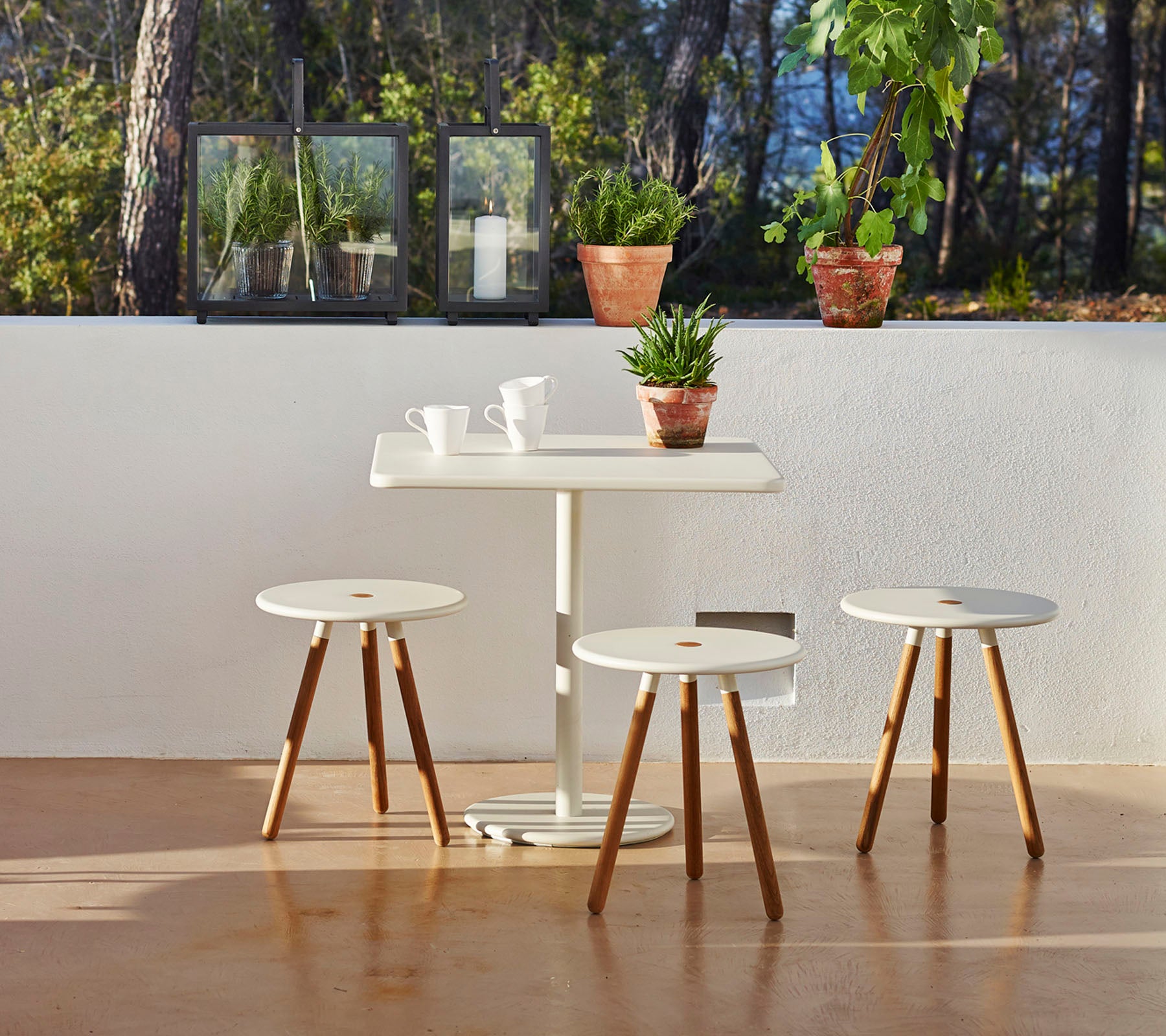 Et minimalistisk bord med tre matchende krakker, omringet av potteplanter som skaper en rolig og innbydende atmosfære.