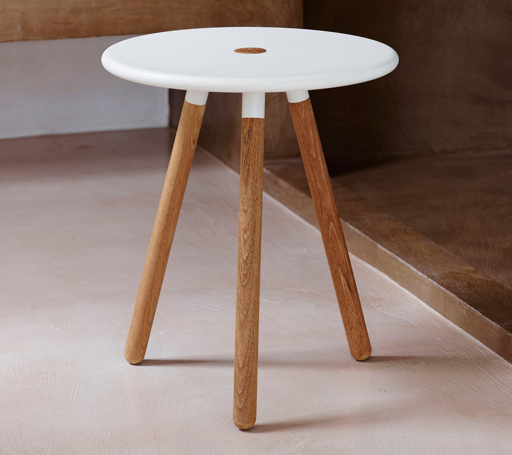Et moderne rundt bord med hvit topp og naturlige treben, med et lite hull i midten for designinteresse.