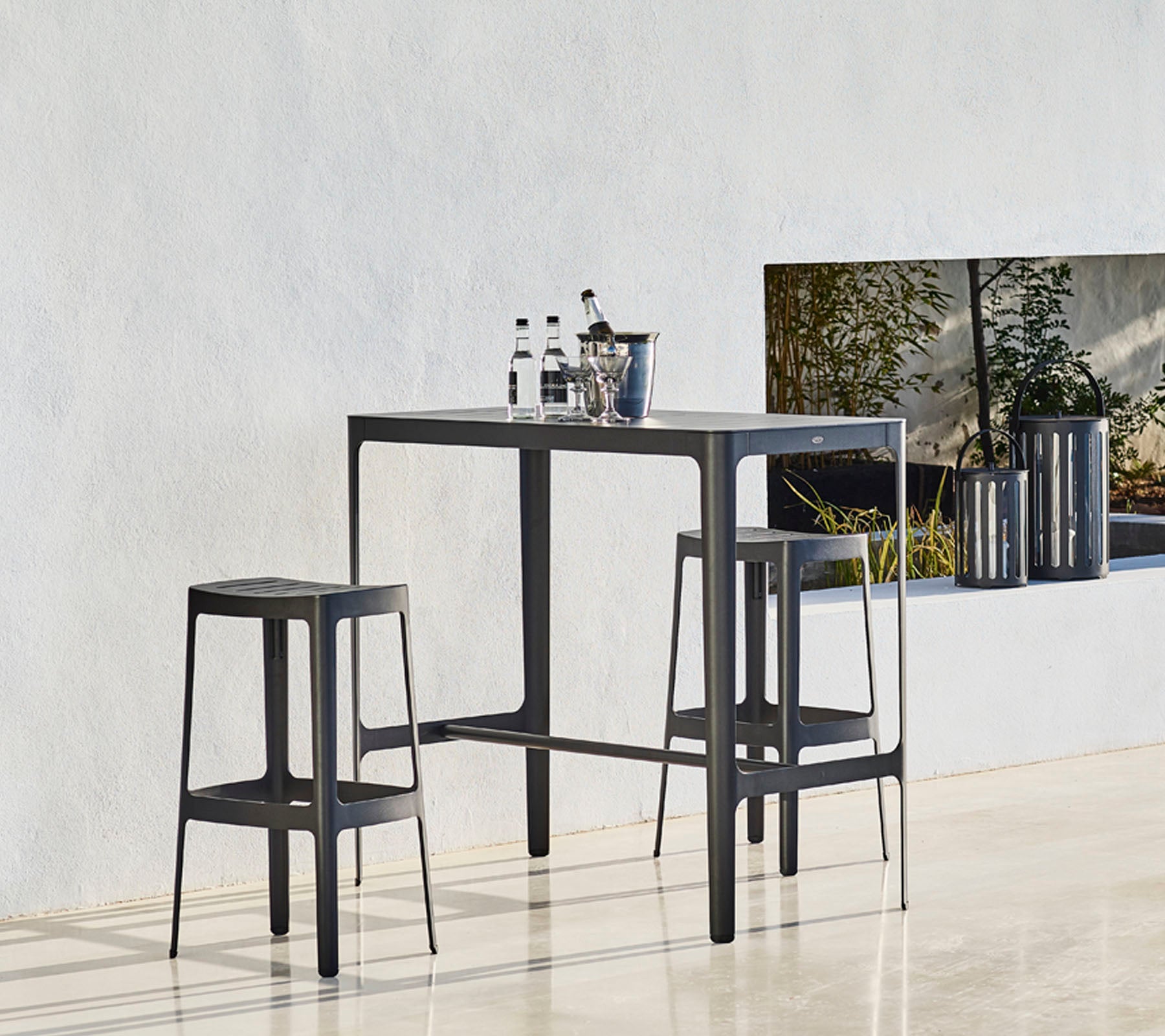 Et stilrent bord med to matchende krakker, med et minimalistisk design og flasker plassert oppå, mot en nøytral bakgrunn.