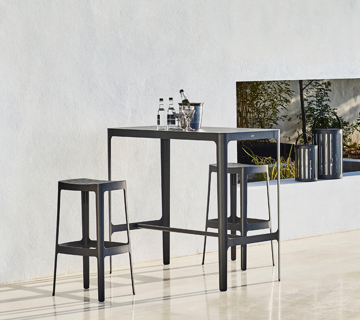 Et stilrent bord med to matchende krakker, med et minimalistisk design og flasker plassert oppå, mot en nøytral bakgrunn.