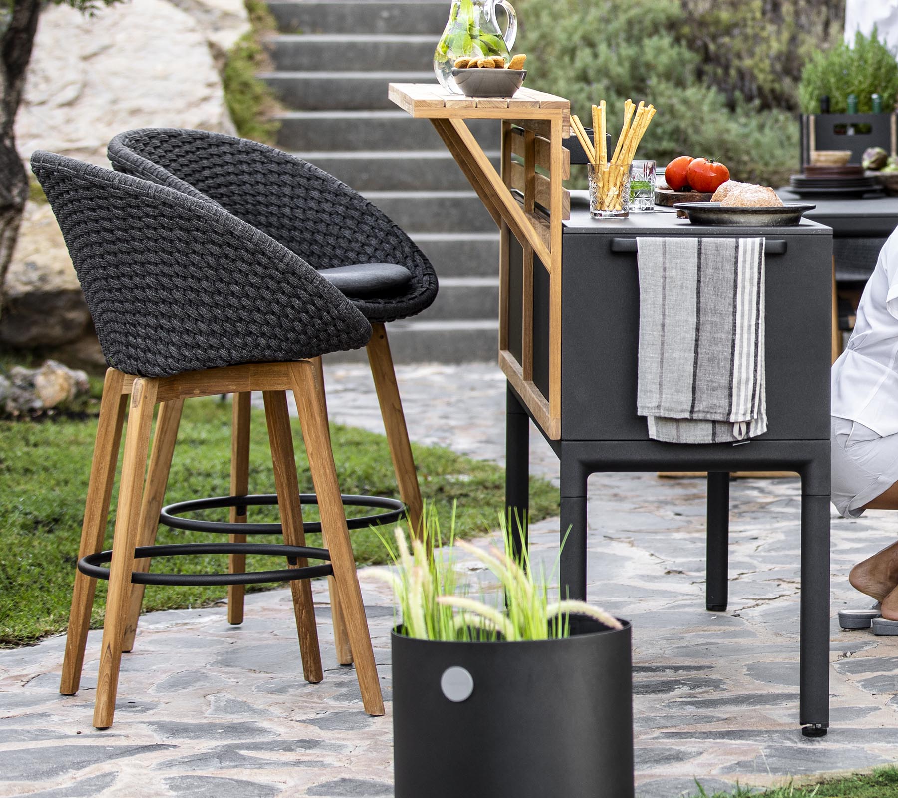 Stilfulle utendørsmøbler med rattan-stoler, en moderne barvogn og ferske ingredienser arrangert på en benkeplate, komplementert med dekorative planter.