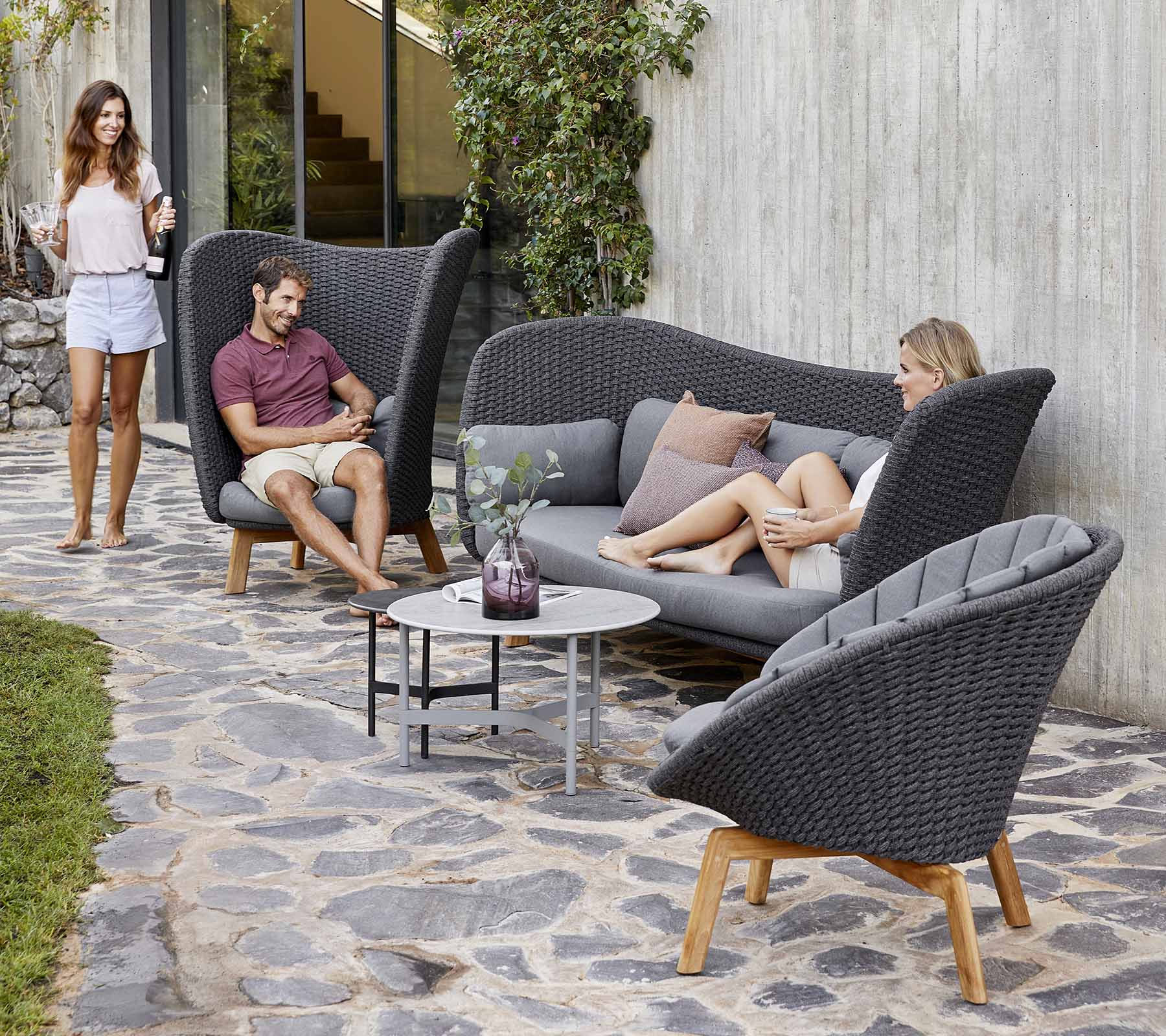 Stilig ute sitteopplegg med en buet sofa og stoler, med et lite bord, omgitt av grøntområder.
