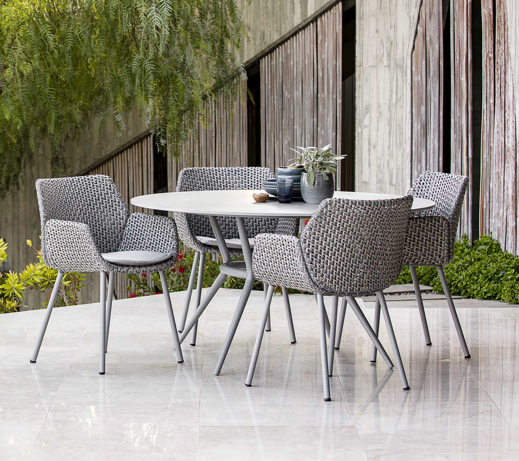 Moderne utendørs spisebordsett med flettede stoler, stylet med planter og borddekor, med en moderne estetikk.