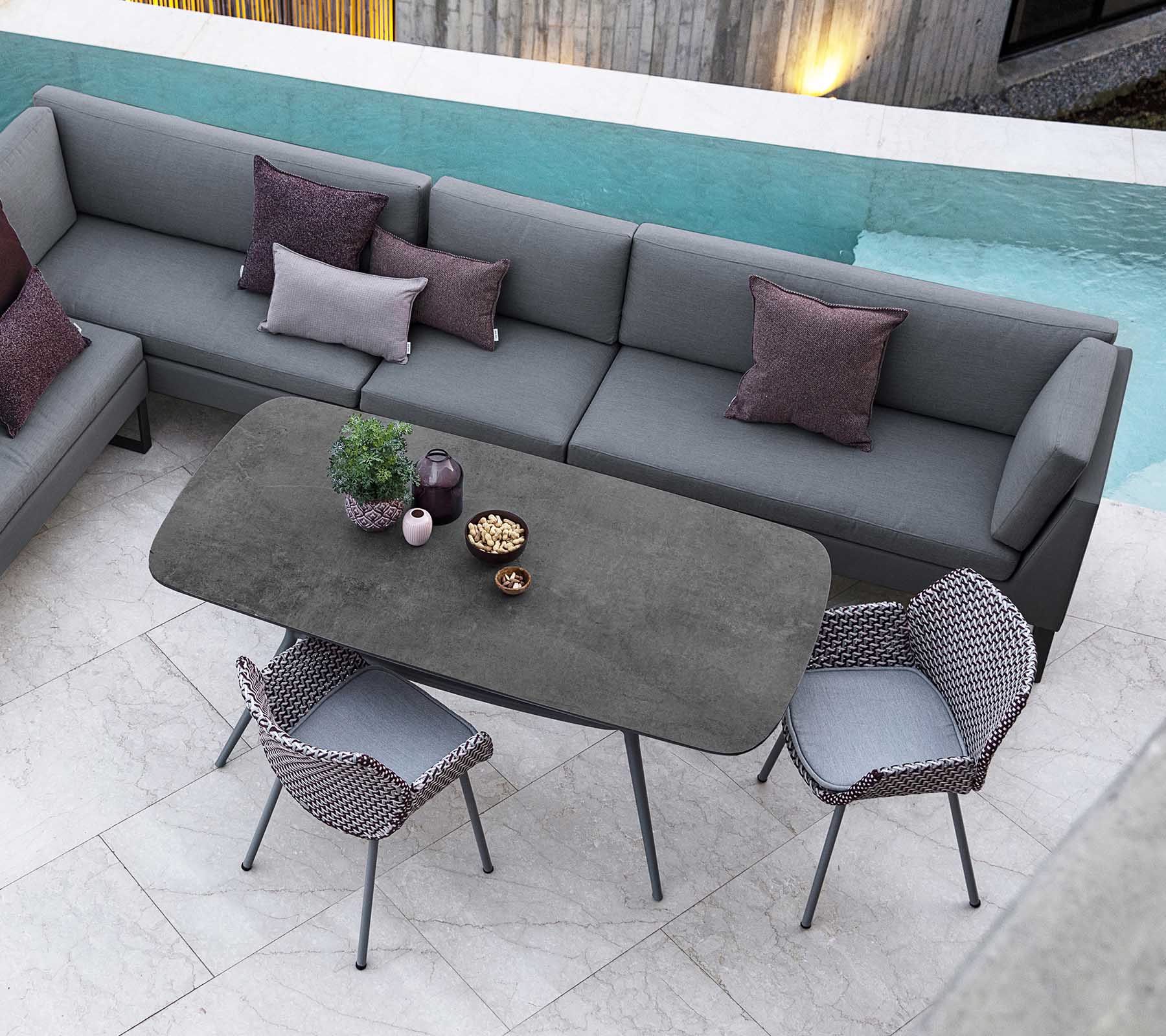 Moderne uteplass med en seksjonalsofa med puter, et stilrent rektangulært bord og stilige stoler, komplettert med utsikt over bassenget.