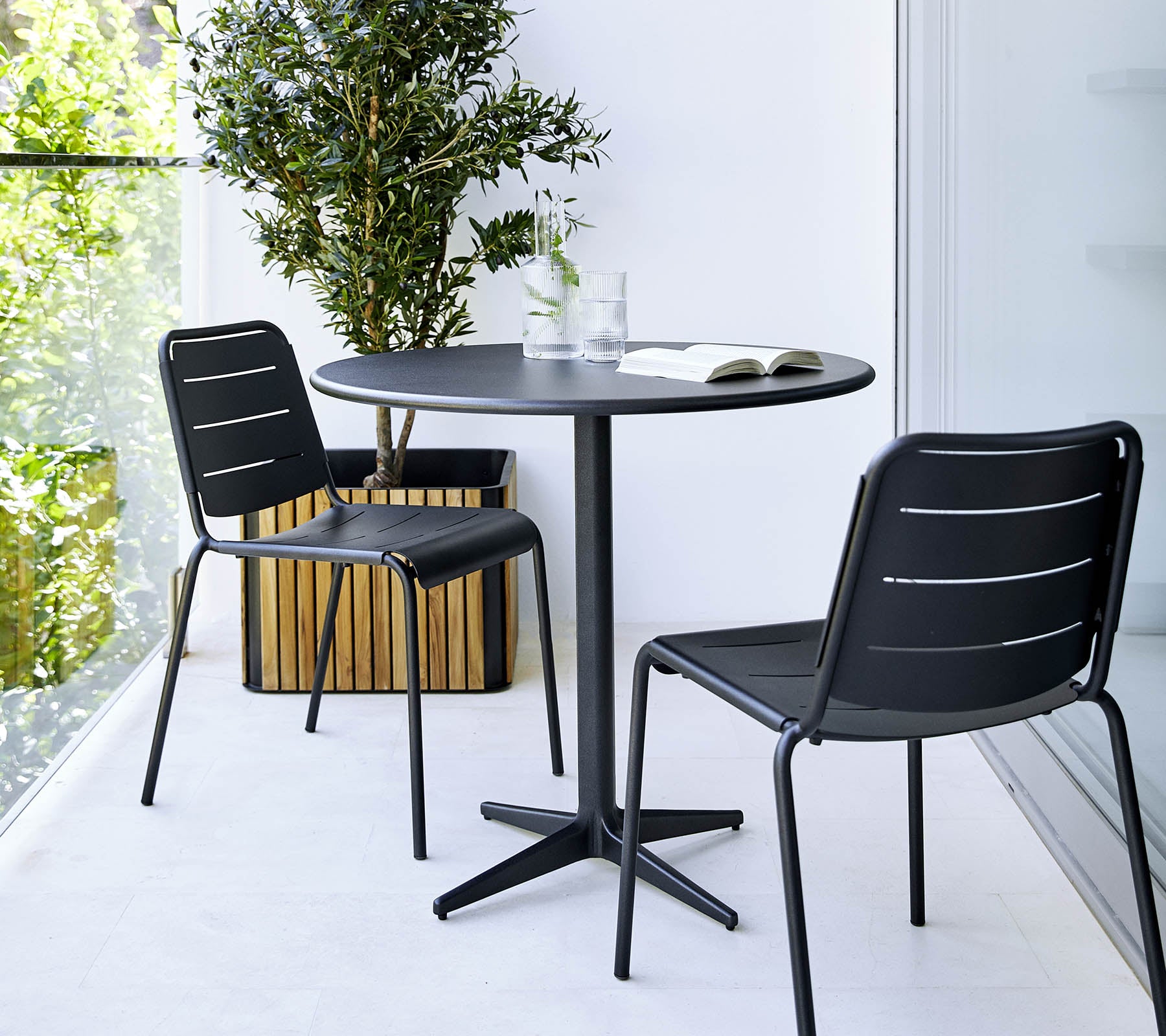 Litet rundt bord med to svarte stoler og en potteplante i nærheten, som skaper en minimalistisk og stilfull atmosfære.