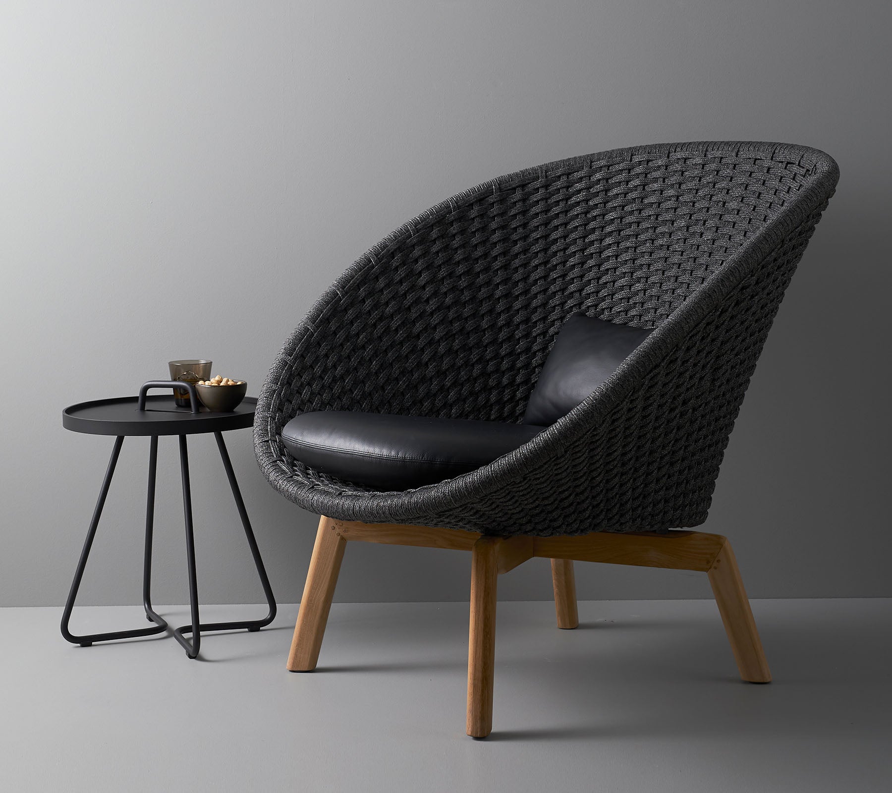 Stilig vevd stol med en svart pute og et moderne rundt sidebord, ideelt for moderne boarealer.
