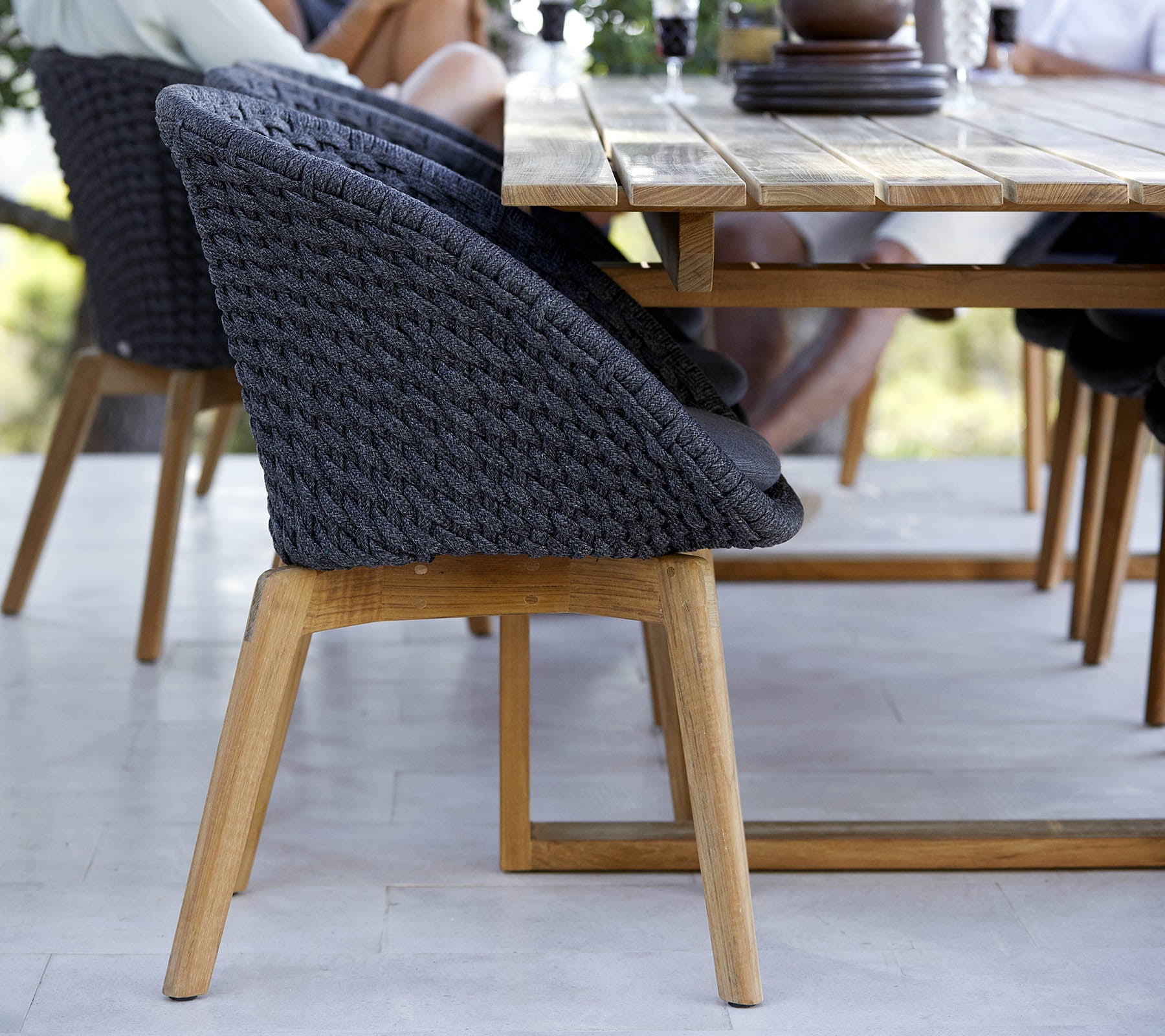 Stilig vevd stol med en treramme, plassert ved siden av et bord, som viser et moderne design perfekt for samlingsområder.