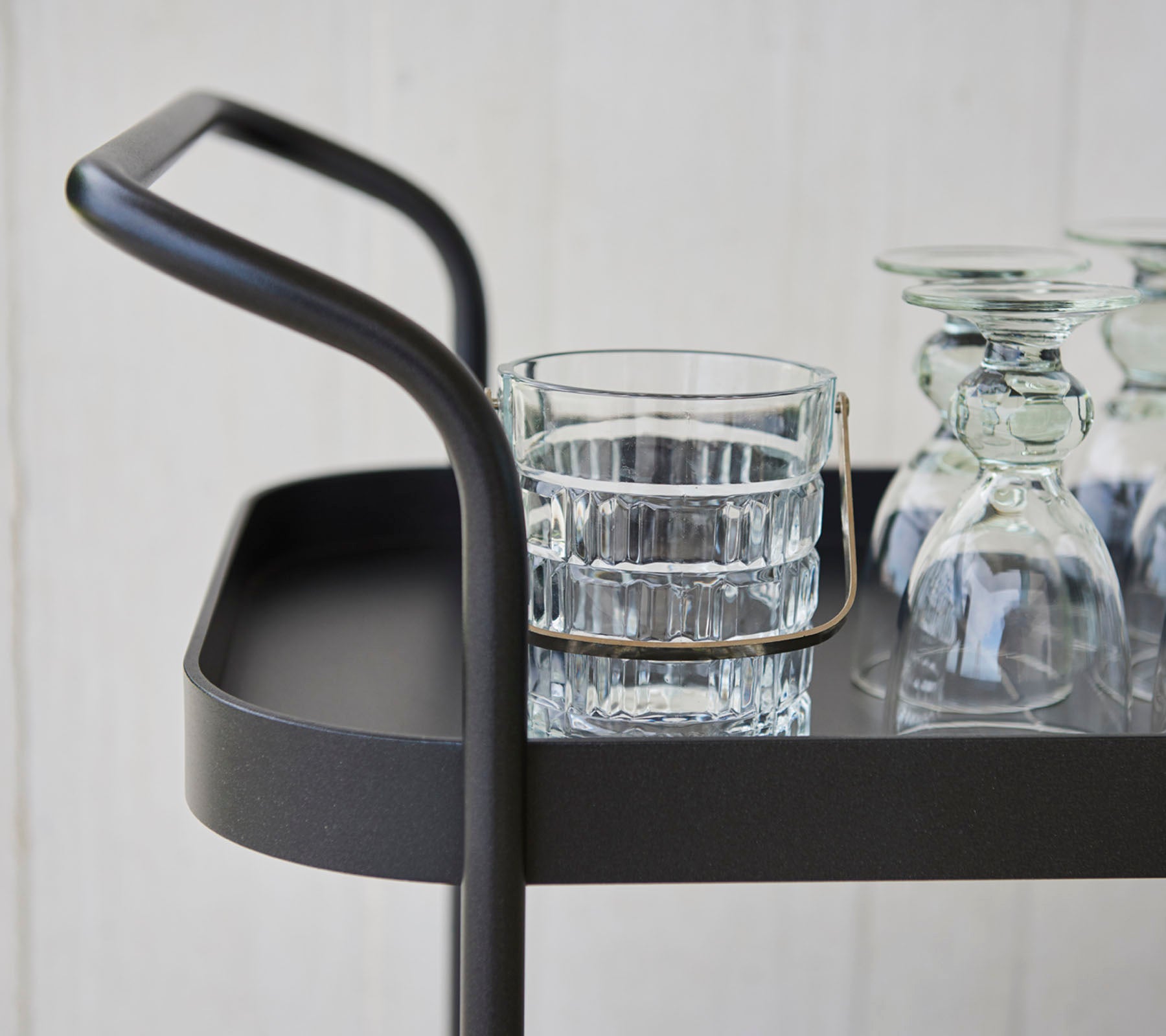 Stilig serveringsvogn med et slankt håndtak, som har et glass og flere klare glasskåler på en flat overflate.