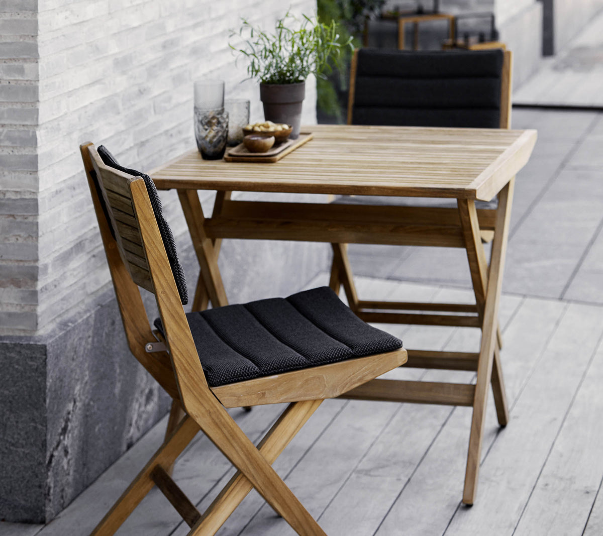 Trekjøkkenbord og stoler med svarte puter, pyntet med potteplanter og dekorativt glass. Perfekt for en koselig setting.