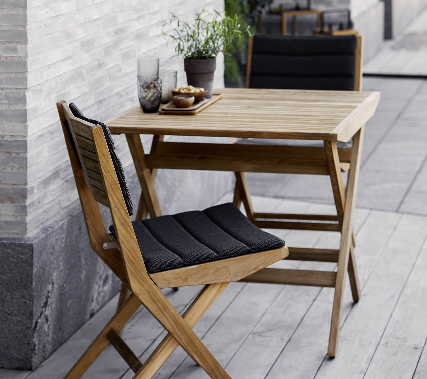 Trekjøkkenbord og stoler med svarte puter, pyntet med potteplanter og dekorativt glass. Perfekt for en koselig setting.