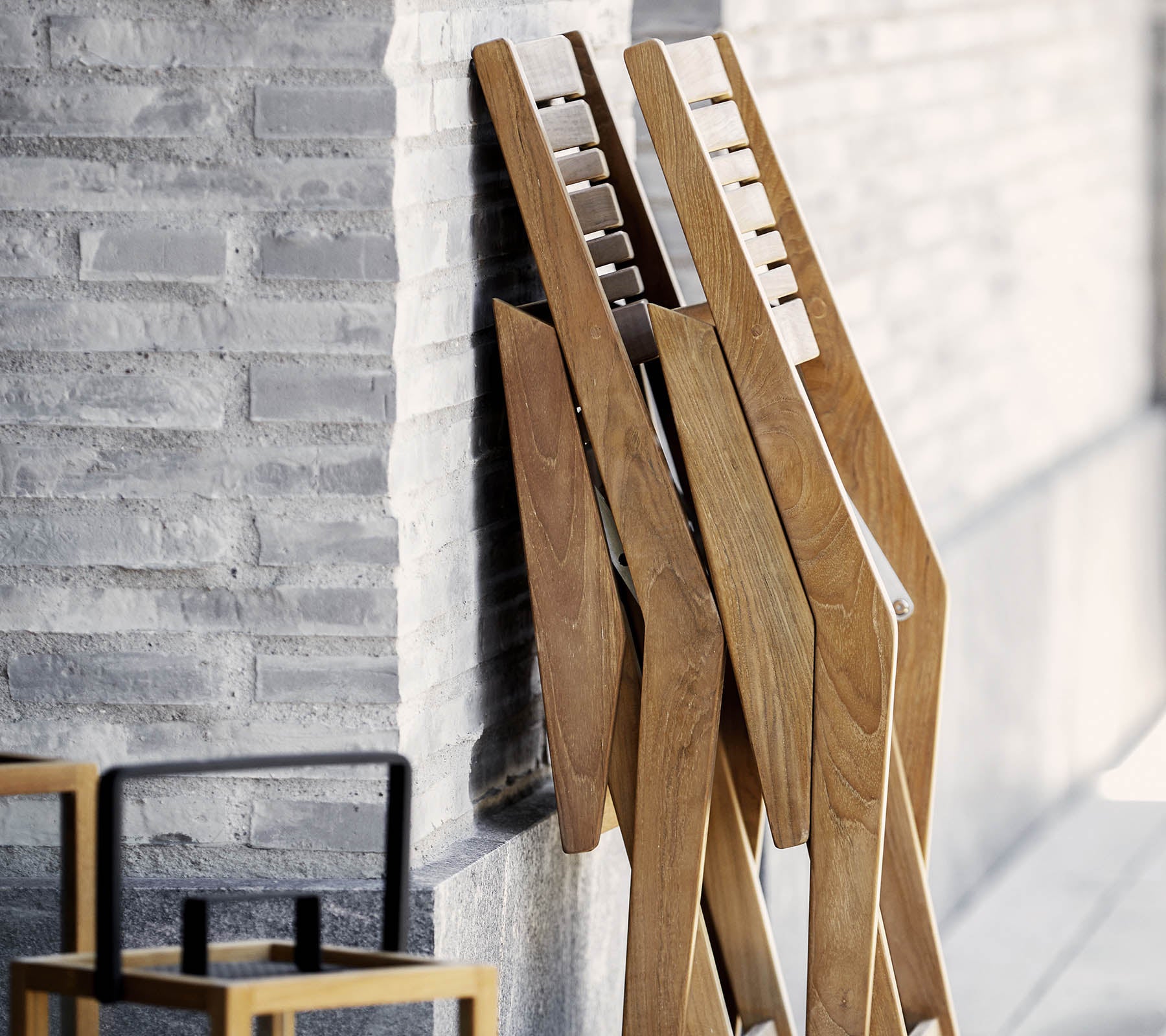 Tre trestativ med et stilrent design, lent mot en teksturert vegg, akkompagnert av en enkel, stilfull stol i forgrunnen.