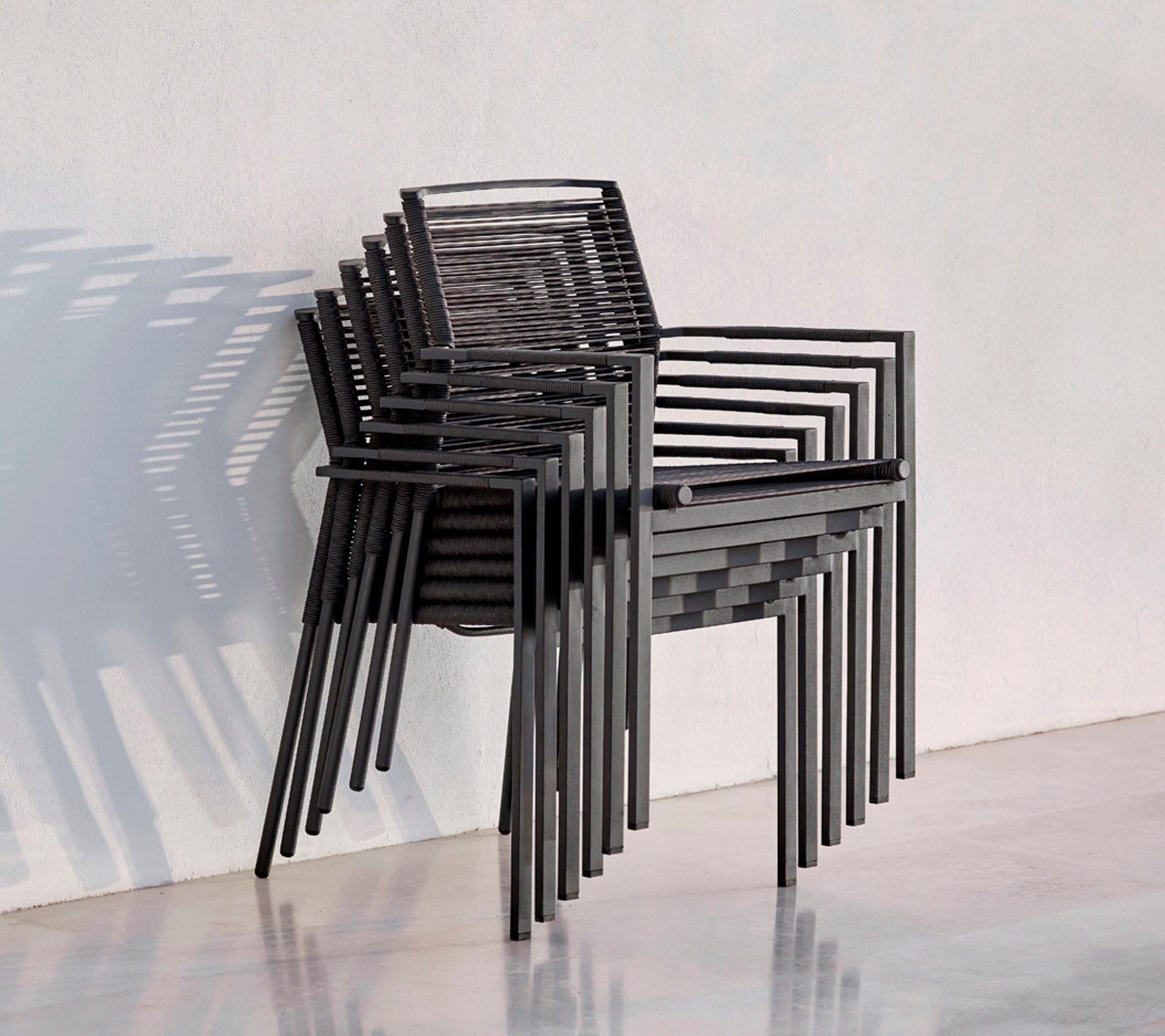 En stabel med moderne svarte stoler med et slankt design, som kaster skygger mot en lys bakgrunn.
