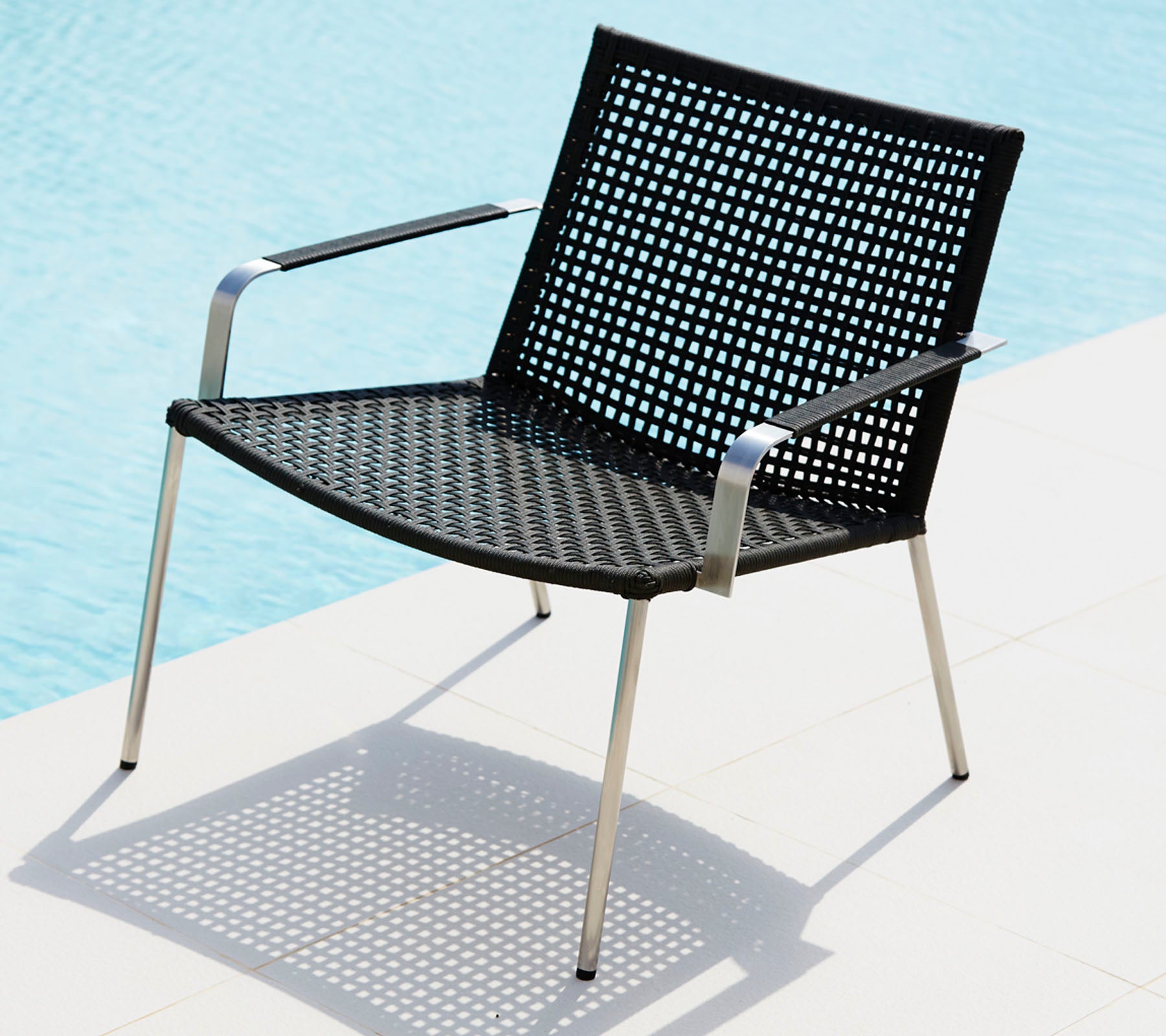Stilig svart stol med perforert design og slanke metallben som kaster skygge på en lys overflate.
