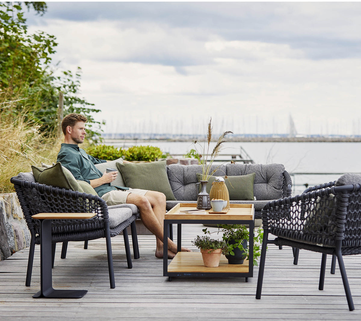 Et komfortabelt sitteområde med en mann som slapper av, med stilige rattanstoler og et trekaffebord prydet med planter og dekorative gjenstander.