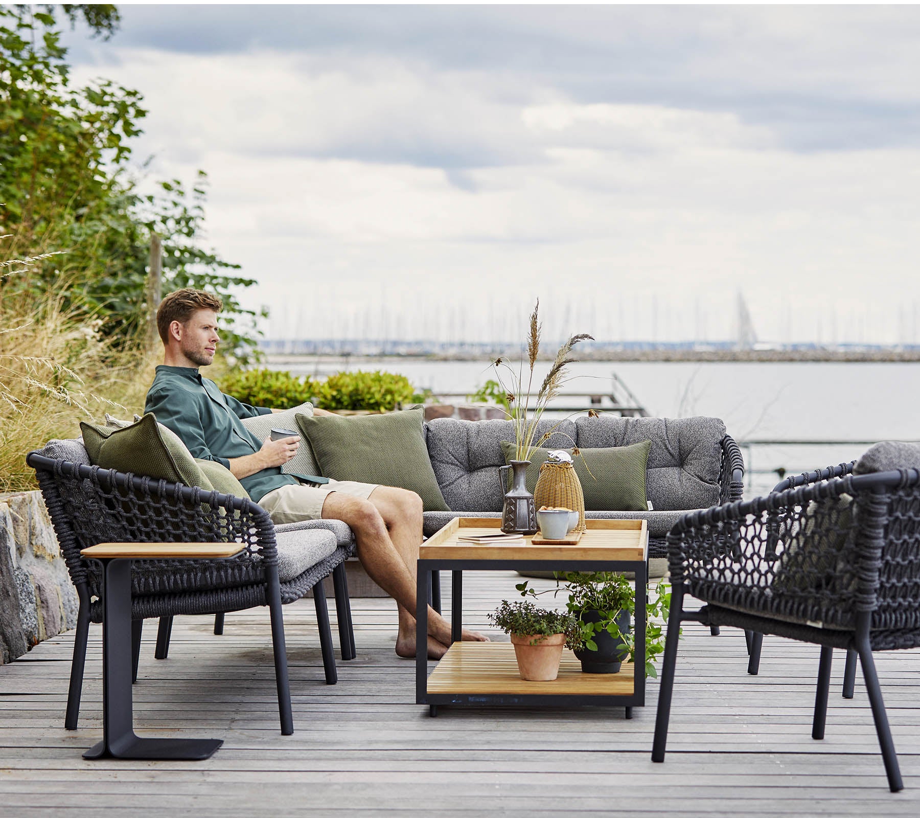 Et komfortabelt sitteområde med en mann som slapper av, med stilige rattanstoler og et trekaffebord prydet med planter og dekorative gjenstander.