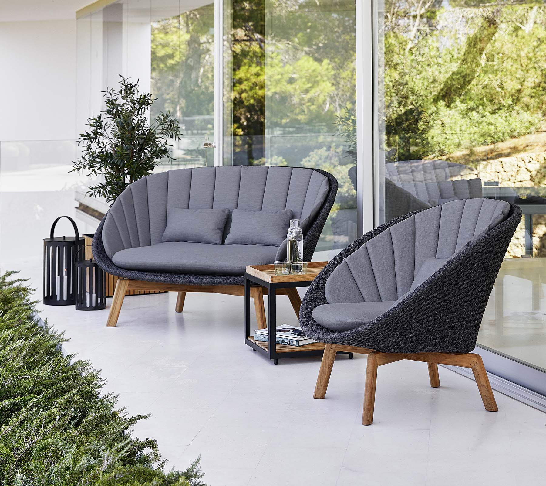 Stilig uteservering med to polstrede stoler og en loveseat, akkompagnert av et lite bord og en dekorativ lampe.