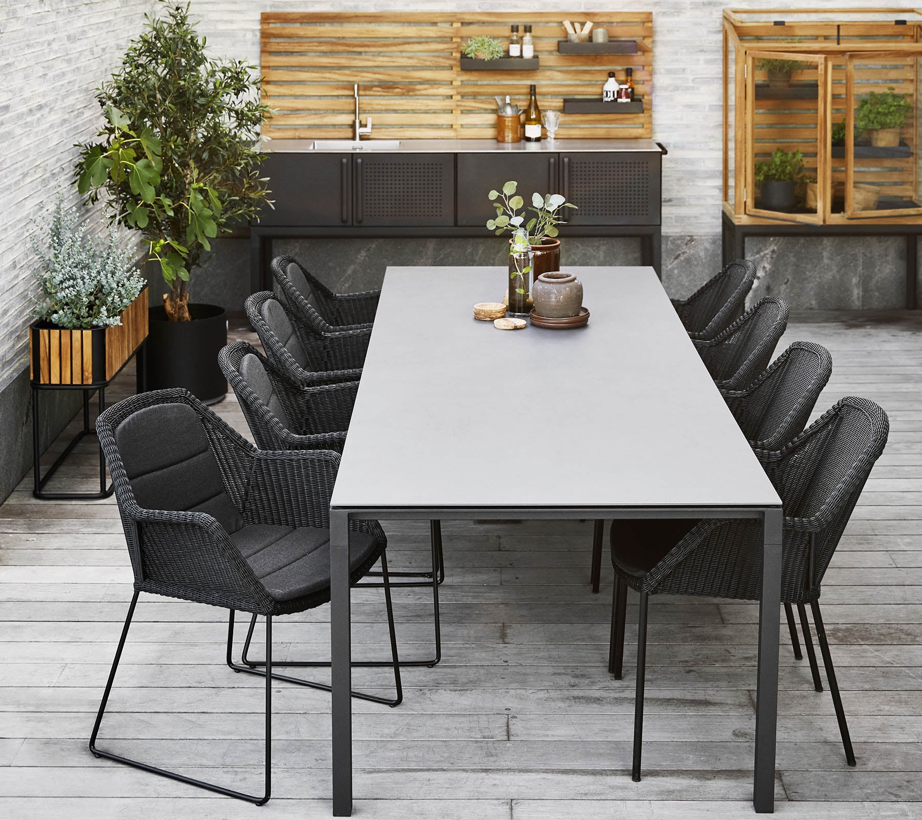Et moderne middagsoppsett med et langt bord omgitt av slanke svarte stoler, komplementert av dekorative planter og en trebakgrunn.