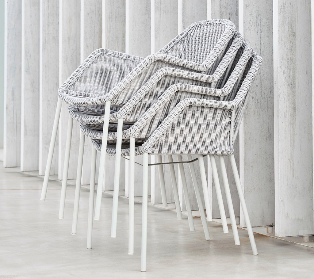 Stablede moderne stoler med et vevd design i grått og hvitt, som hviler mot vertikale flater, og viser en slank og minimalistisk estetikk.