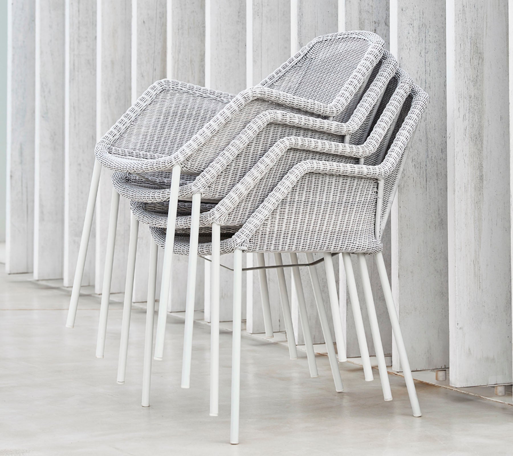 Stablede moderne stoler med et vevd design i grått og hvitt, som hviler mot vertikale flater, og viser en slank og minimalistisk estetikk.