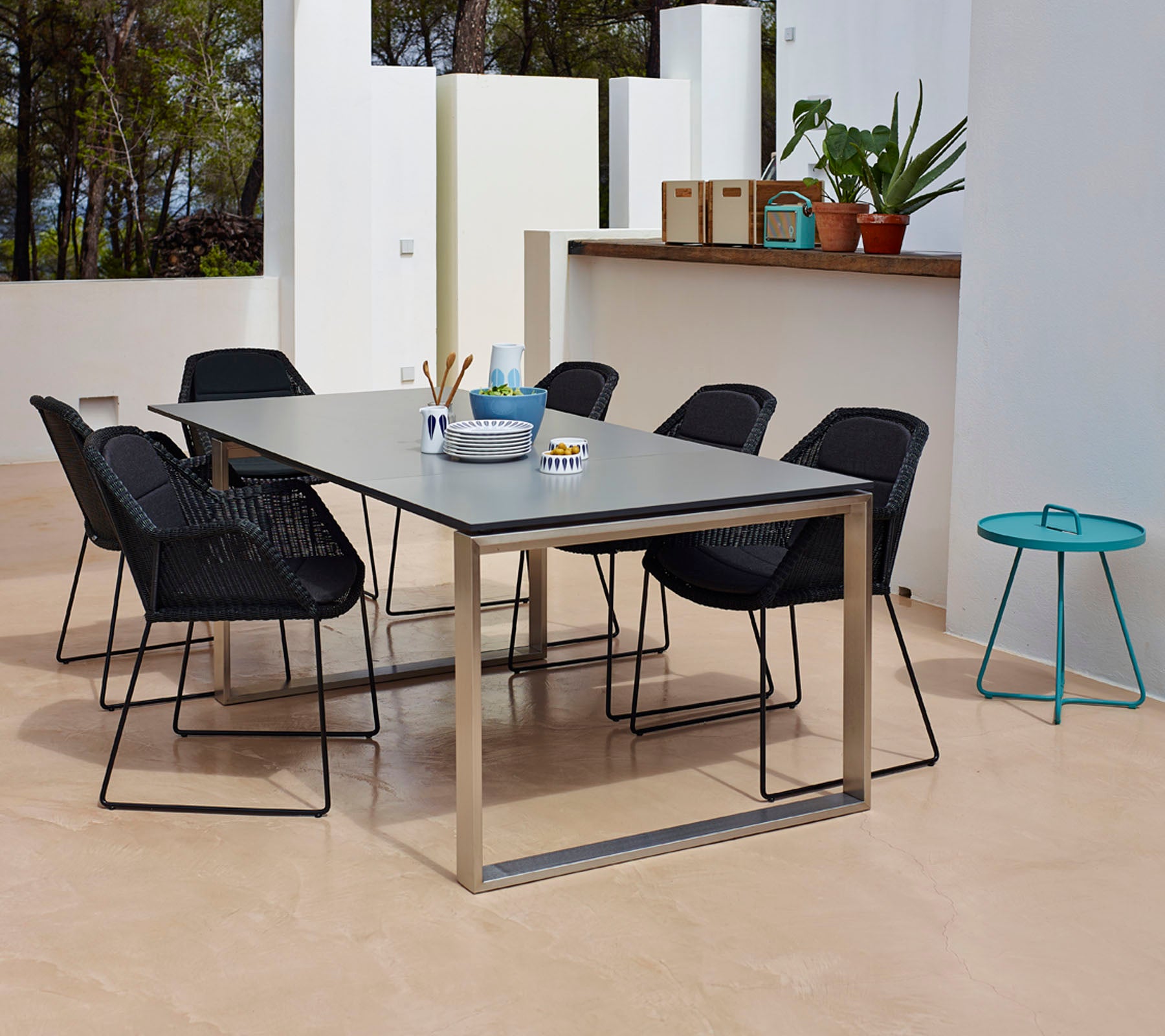 Et moderne spiseoppsett med et rektangulært bord med en glatt overflate, omgitt av seks svarte flette stoler og et lite teal sidebord.