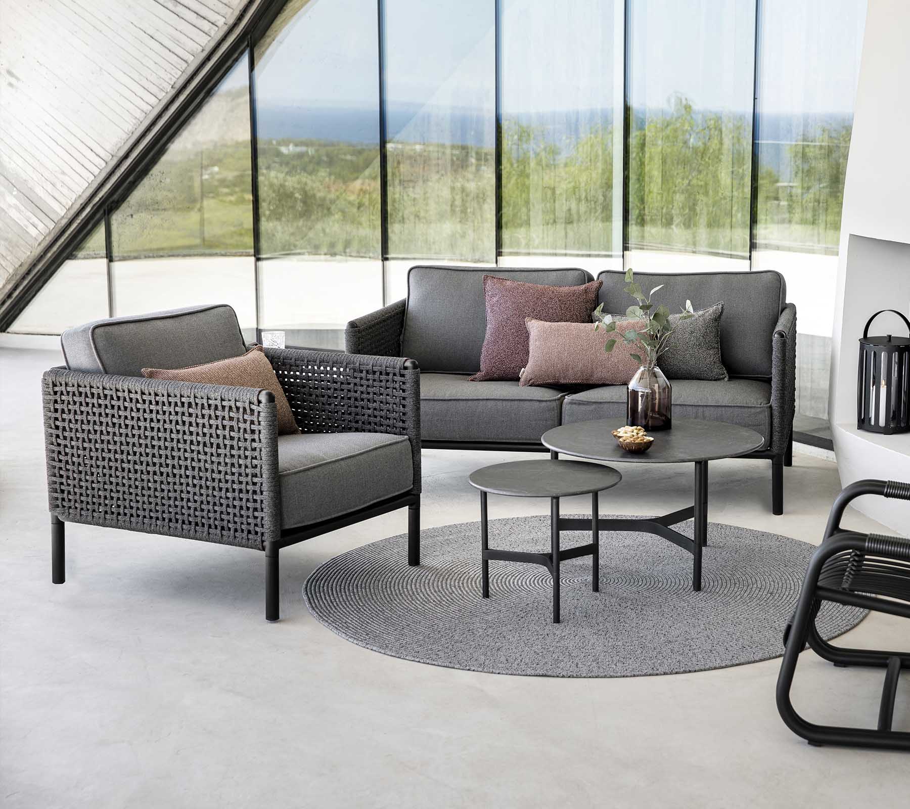 Stilig sittearrangement med en grå sofa og lenestol med puter, ledsaget av et rundt bord på et strukturert teppe.