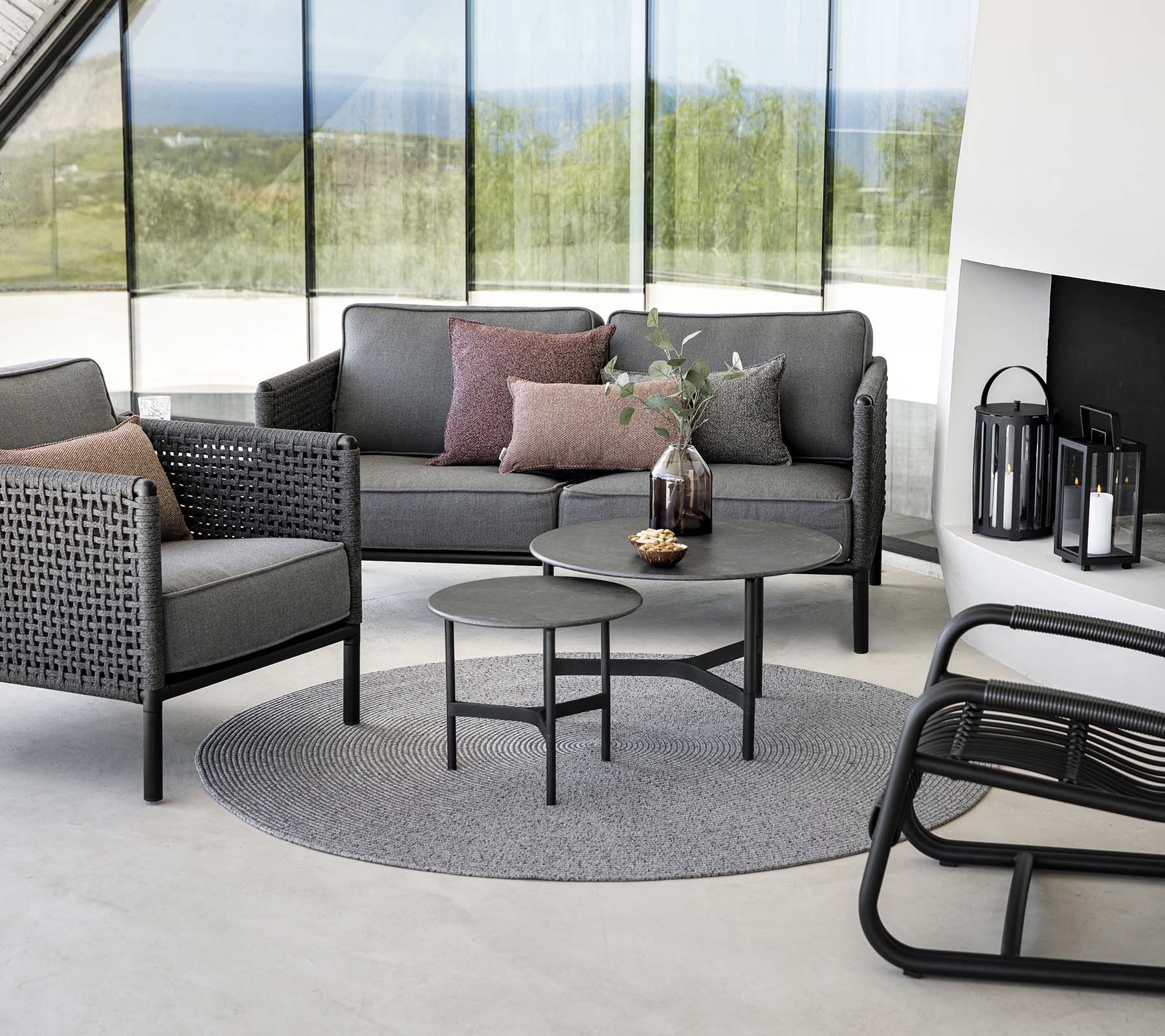 Stilig sitteområde med en grå sofa med puter, rundt sofabord og aksentstoler på et rundt teppe. Naturlig lys forbedrer stemningen.