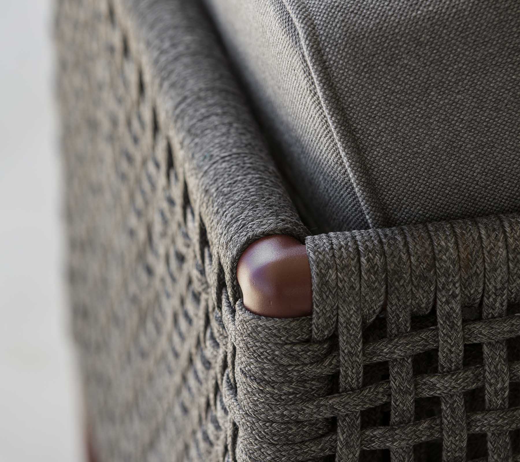 Nærbilde av et flettet møbelhjørne som har elegant grått stoff og glatte tre detaljer, som viser en blanding av tekstur og stil.