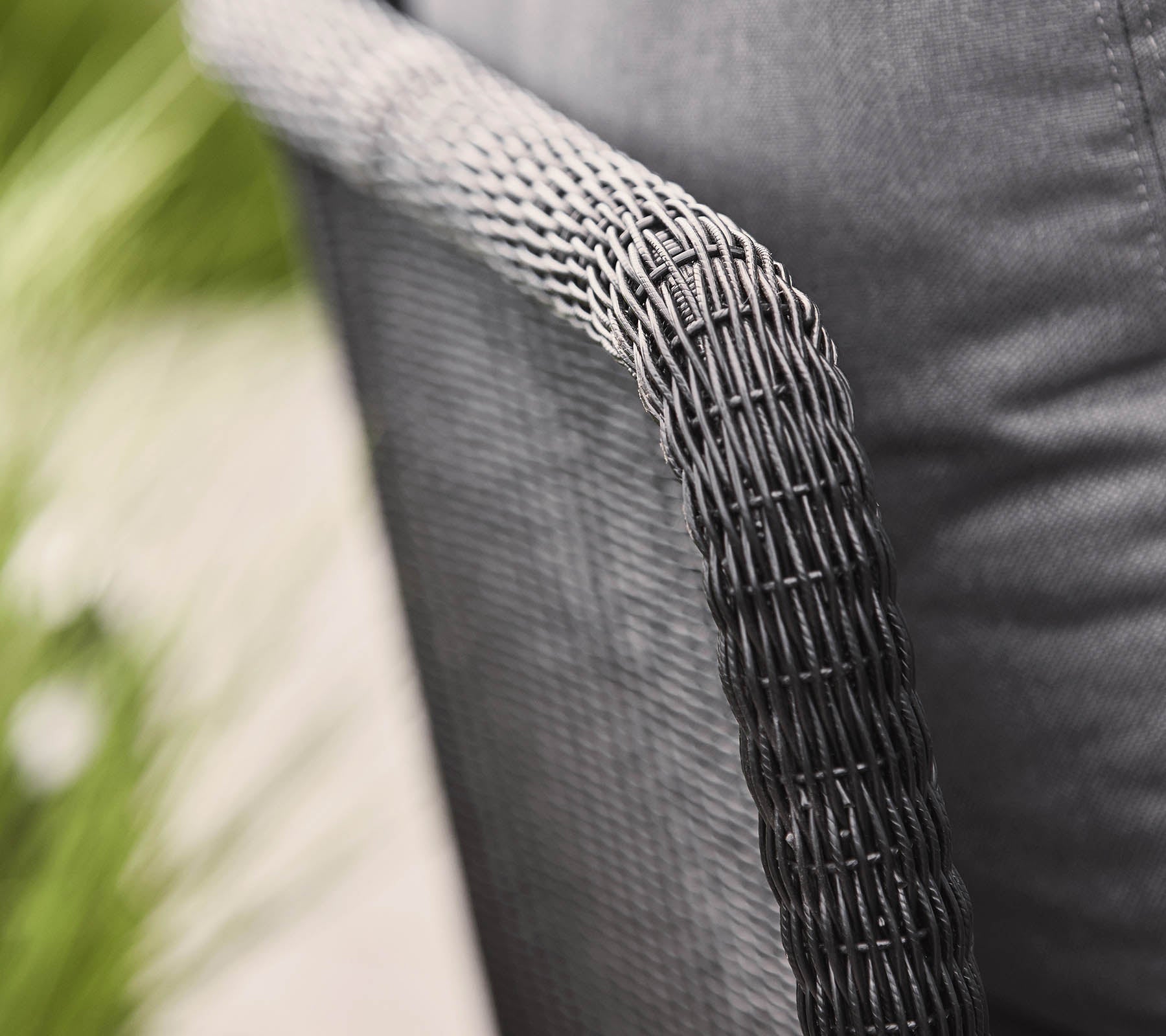 Nærbilde av et vevd stolarm med en teksturert svart finish, som viser et moderne design og en koselig stoffsete.