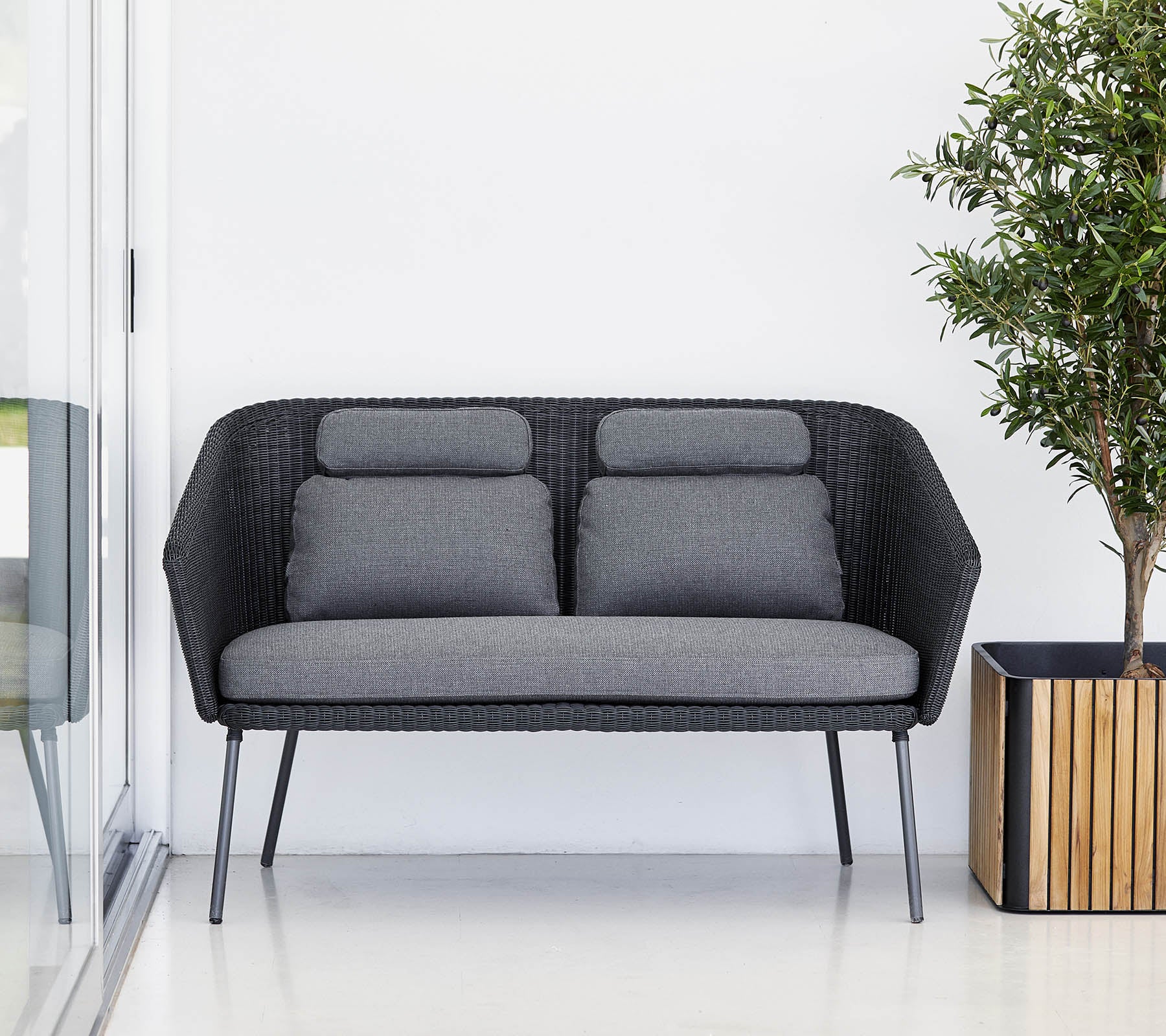 Stilig svart sofa med grå puter, komplementert av en potteplante i en trekrukke. Moderne og minimalistisk design.