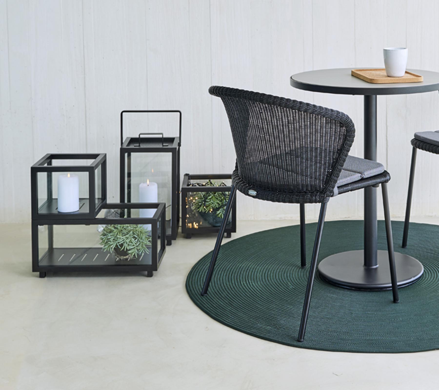 Moderne sitteplasser og dekorative glasslanterner med planter, arrangert rundt et rundt bord, på et rundt grønt teppe.